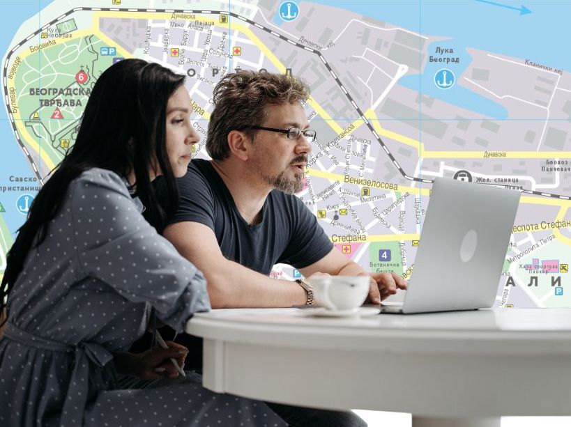 Roditelji traže stan na laptopu i plan grada Beograda u pozadini